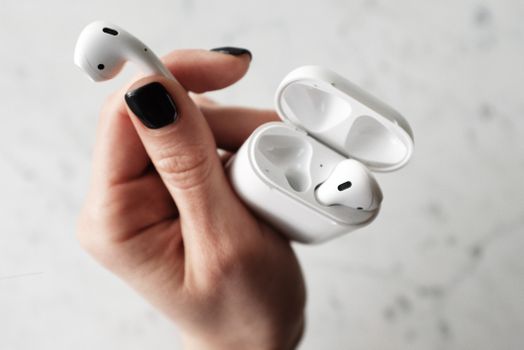 A detailed close-up of white wireless earbuds held in a hand with black nail polish.