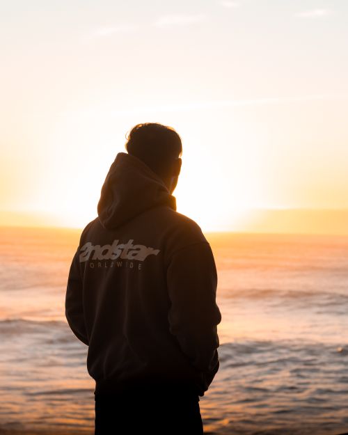 Free A man in a hoodie watches the sunrise by the ocean, capturing a peaceful Sydney morning. Stock Photo
