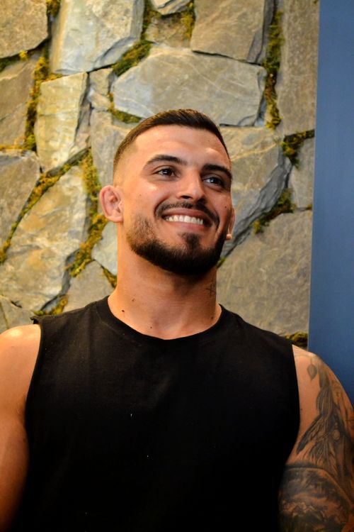 Free A smiling man with tattoos poses indoors against a stone wall. Stock Photo