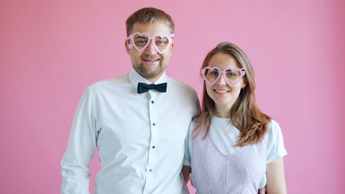 Free Happy couple with heart-shaped glasses against pink background. Stock Photo