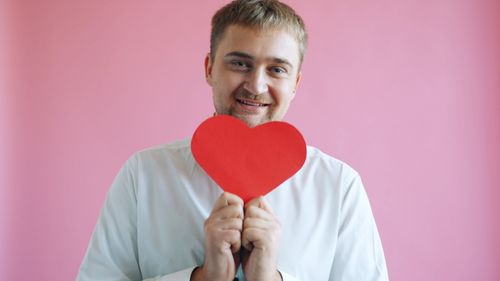 Free Man in white shirt holding a red heart symbol against a pink background. Stock Photo