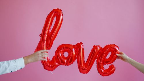 Free Hands holding red love-shaped balloons on a pink backdrop. Perfect for Valentine's Day themes. Stock Photo