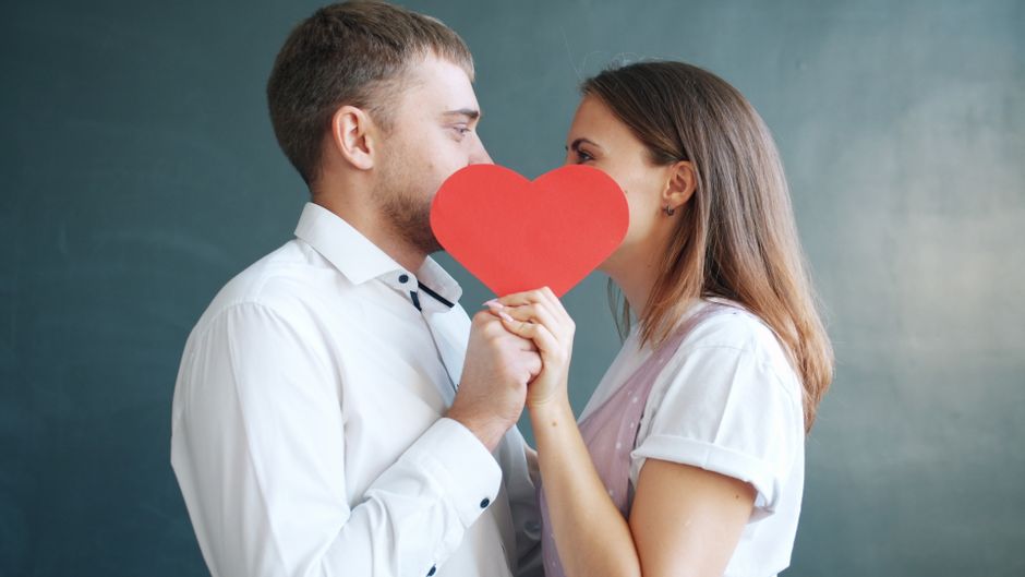 사랑에 빠진 한 커플이 붉은 하트 모양 뒤에서 서로를 껴안고 있어 로맨스와 애정이 넘쳐흐른다.