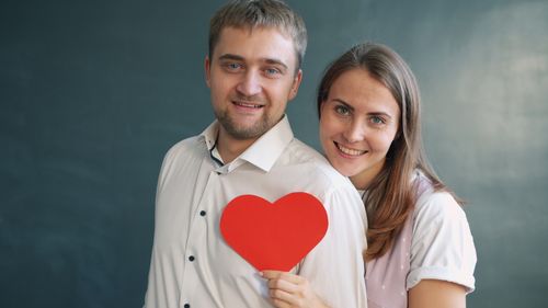 Free Smiling couple embracing and holding a red heart symbol indoors. Stock Photo