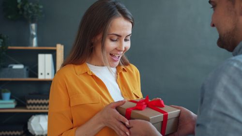 Free A woman delightedly receives a gift box with a red ribbon indoors. Stock Photo