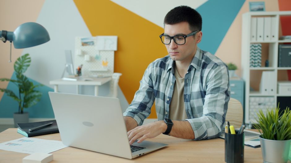 Focused young man wearing glasses, working on a laptop in a stylish office. Focused young man wearing glasses, working on a laptop in a stylish office.