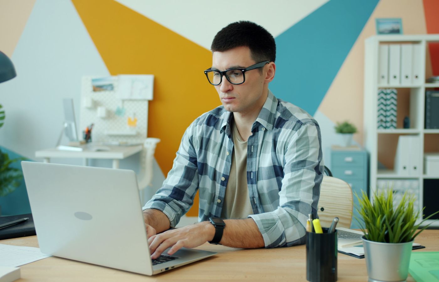 Young adult man working on a laptop in a modern office with colorful decor.