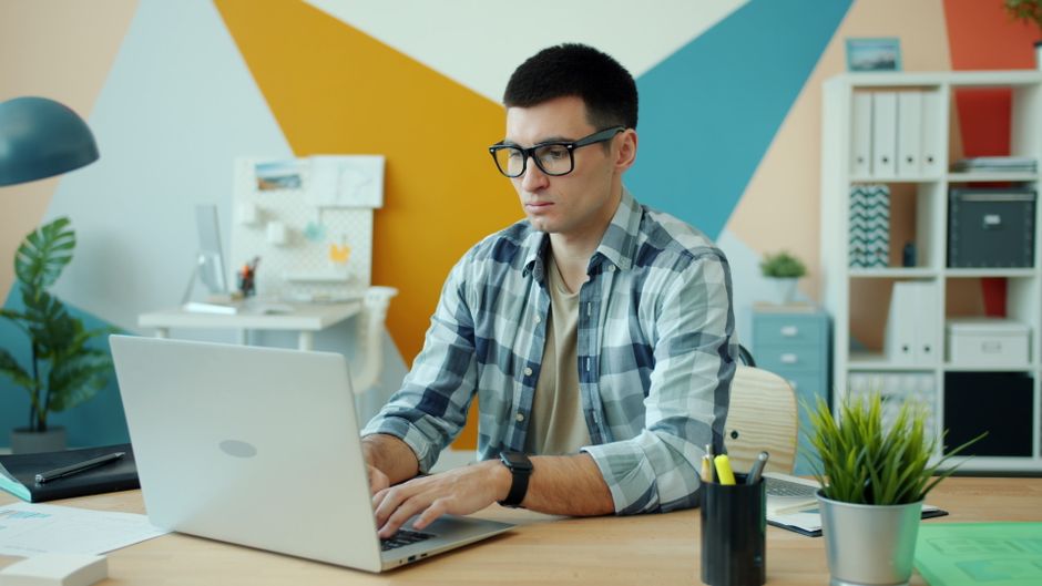 Young adult man working on a laptop in a modern office with colorful decor.