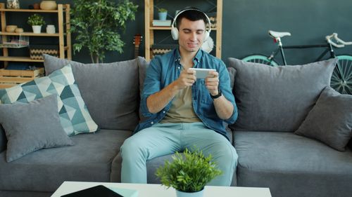 Free Young man enjoying leisure time on couch, playing games with headphones. Stock Photo