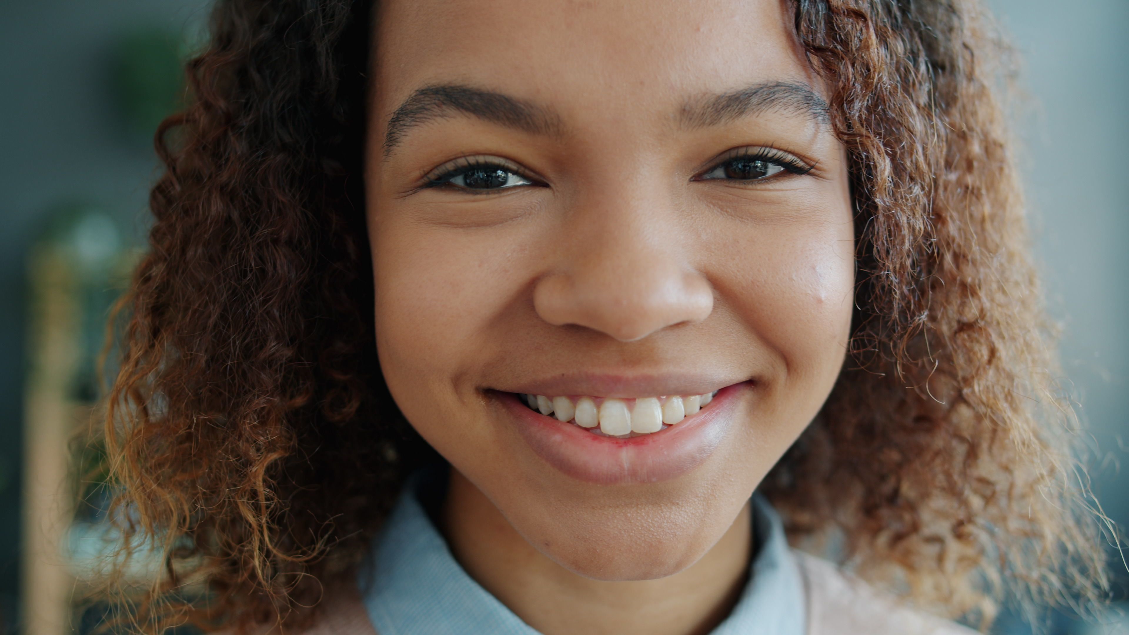 A close-up portrait of a young woman smiling indoors.