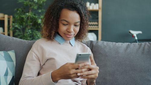 Free Young woman using a smartphone while sitting on a couch indoors. Stock Photo