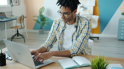 Free Focused young adult working on laptop in modern office setting. Stock Photo