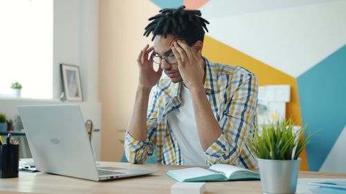 Free Young adult feeling stressed at desk with laptop, in modern office setting. Stock Photo