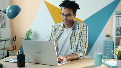 Free Young man in a stylish office using a laptop, embodying modern work environment. Stock Photo