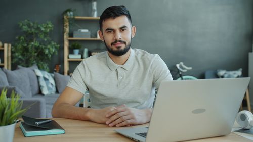 Free A young man sits in a modern home office setting, working on a laptop. Stock Photo