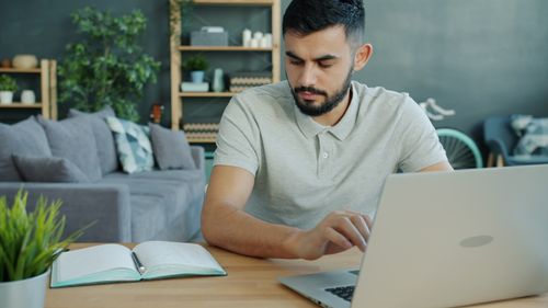 Free Focused man using laptop at home office desk, working on business projects. Stock Photo