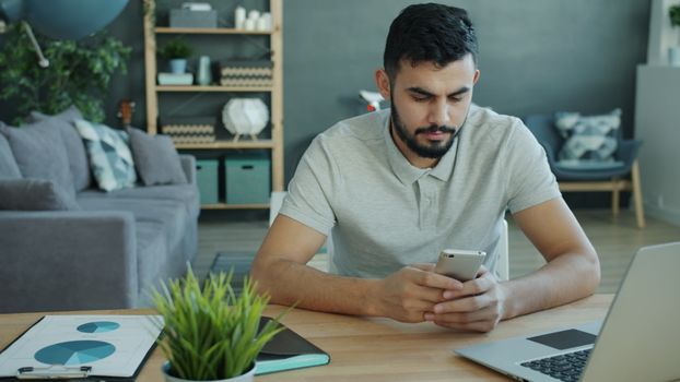 Focused young man working from home using smartphone at desk.