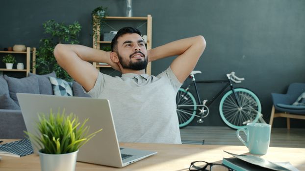 Young man relaxing at home office desk with laptop and bicycle in background.
