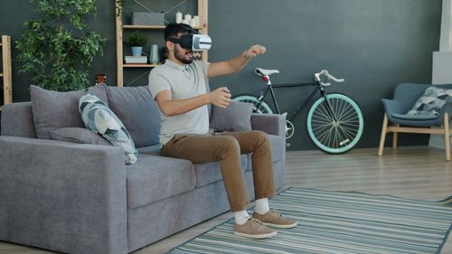 Free A man wearing a VR headset experiences virtual reality while seated on a sofa in a contemporary living room. Stock Photo