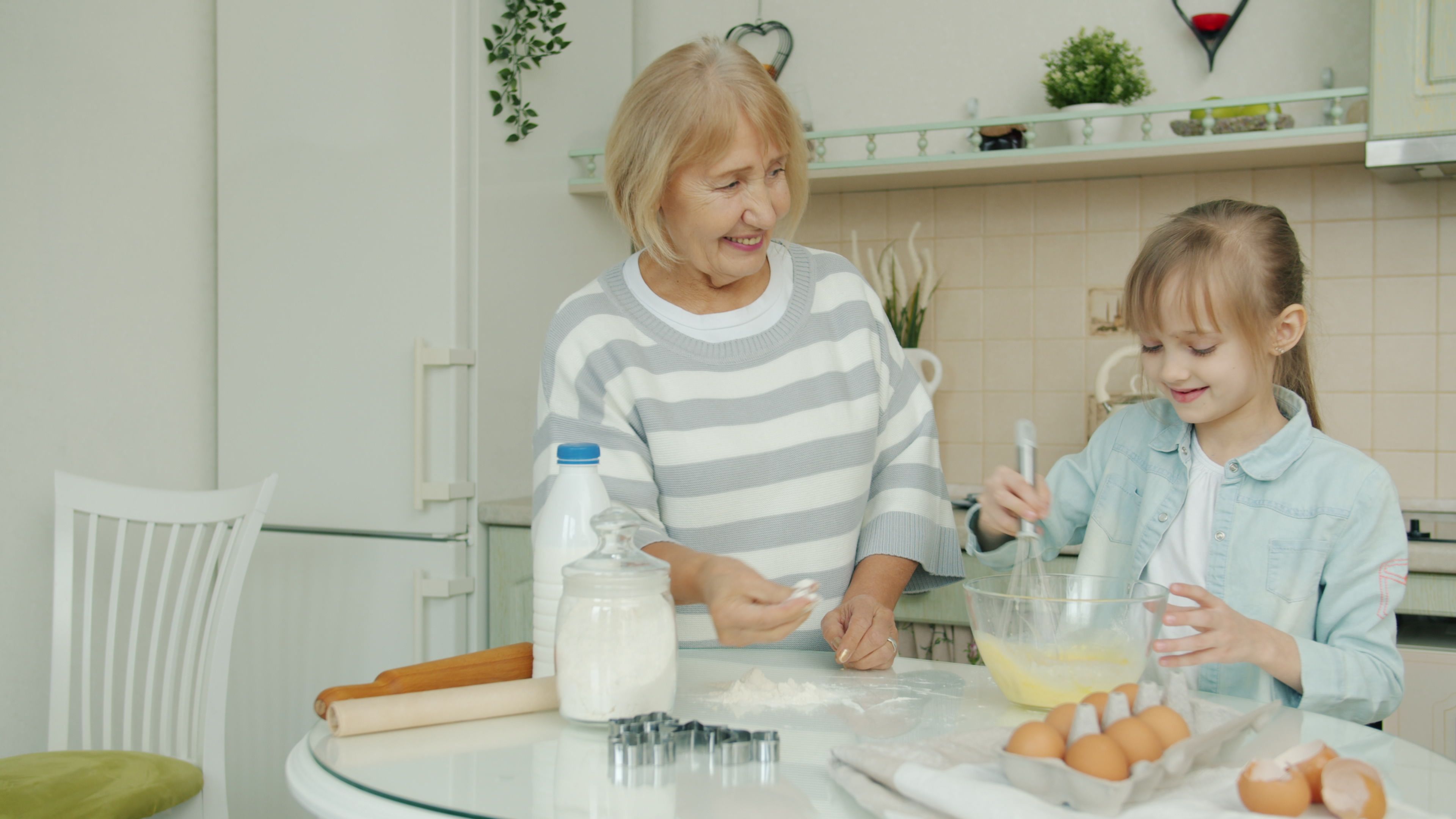 Grandmother and granddaughter enjoy baking in a home kitchen, mixing batter.