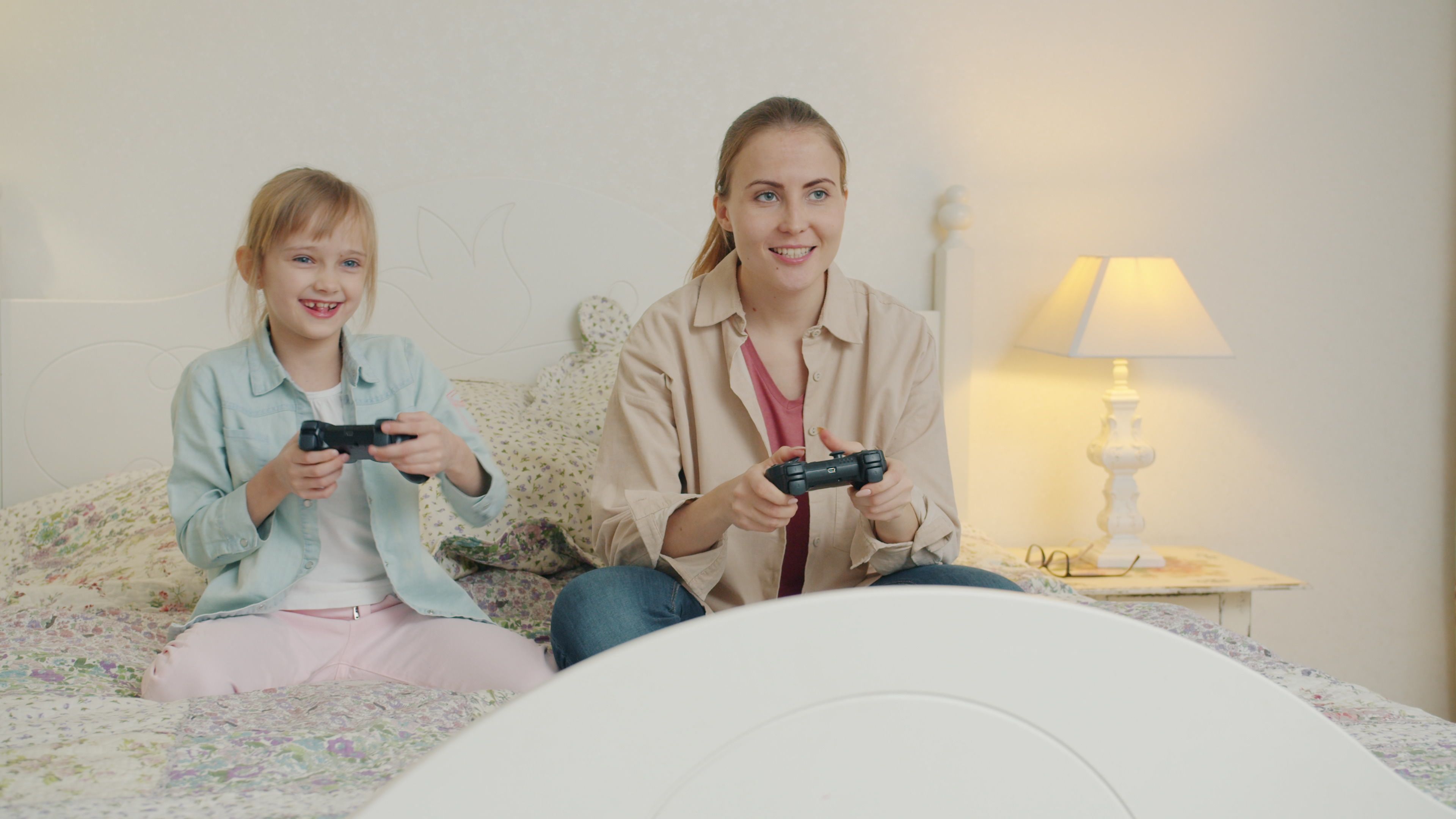 A mother and daughter enjoy playing video games together in a cozy bedroom setting.