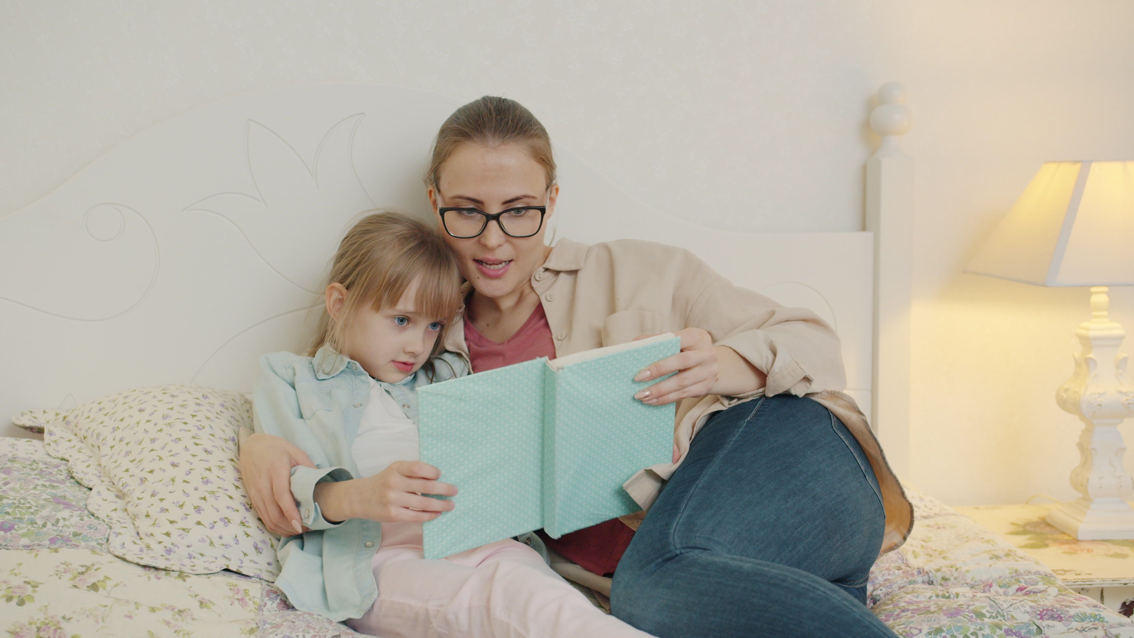 A mother and her young daughter share a cozy reading moment on the bed.