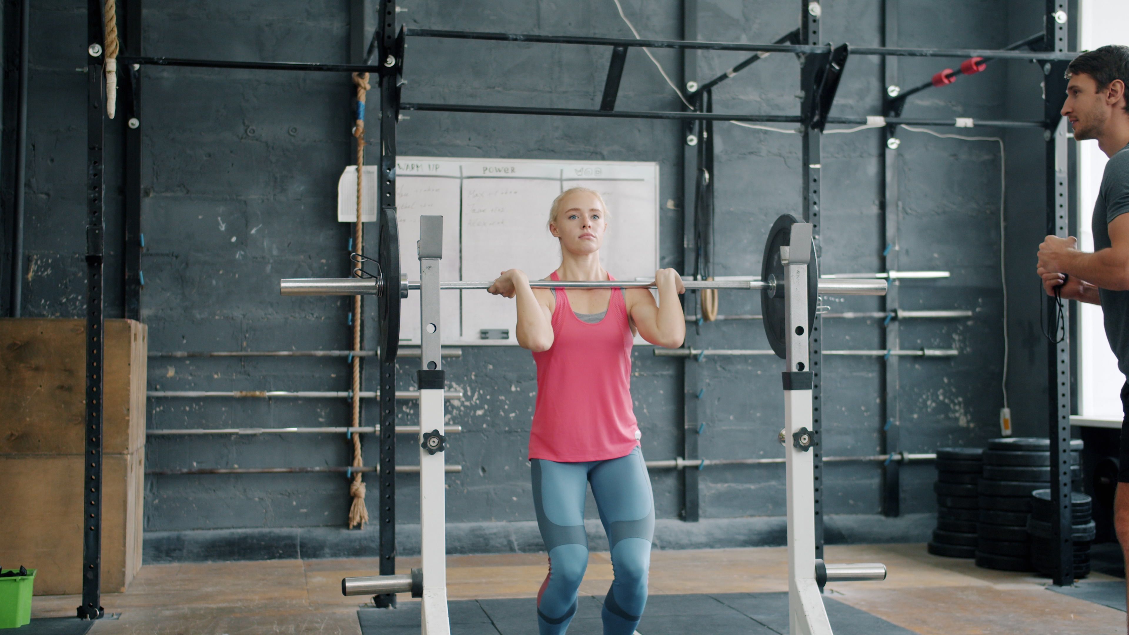 footballer performing barbell squats in a professional training facility, focused coaches observing