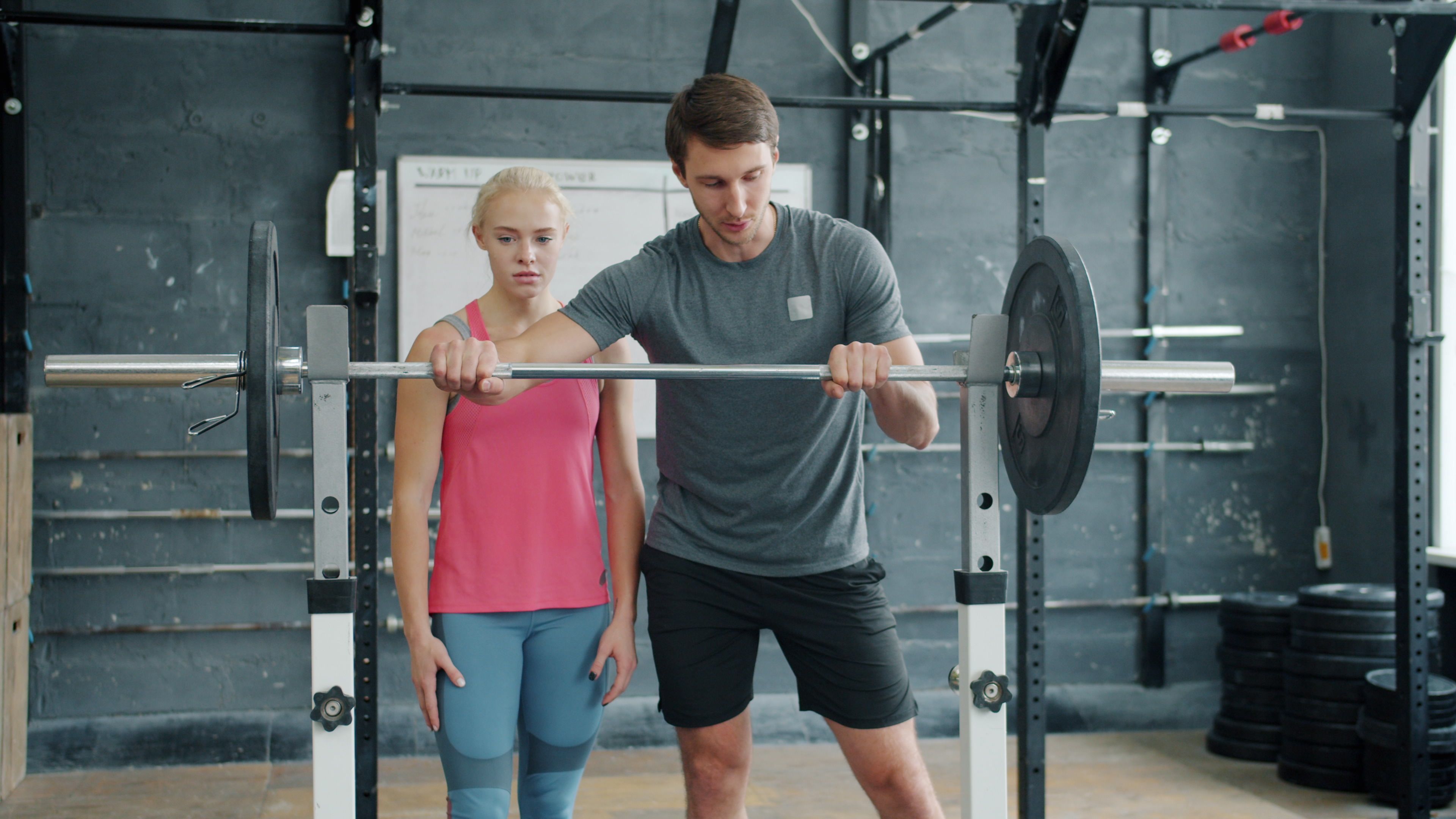 A fitness trainer assists a young woman with weightlifting techniques in a gym setting.