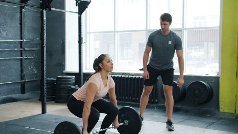 A coach watches a member set up for a deadlift