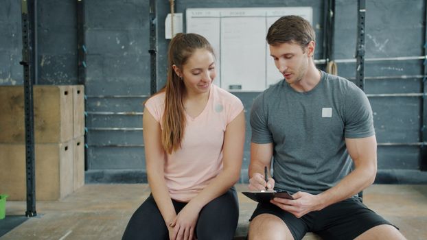 A personal trainer discusses workout goals with a female client at the gym, focusing on fitness plans.