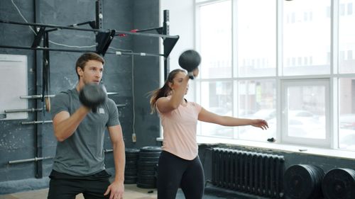 Free Two adults perform an intense kettlebell workout in a modern gym setting. Stock Photo