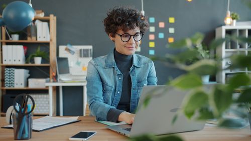 Free Smiling woman working on laptop in a creative home office space. Stock Photo