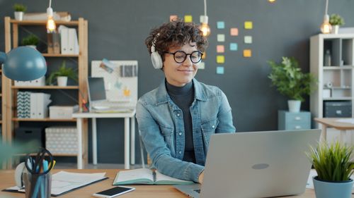 Free Young woman in a cozy home office working on a laptop, wearing headphones. Stock Photo