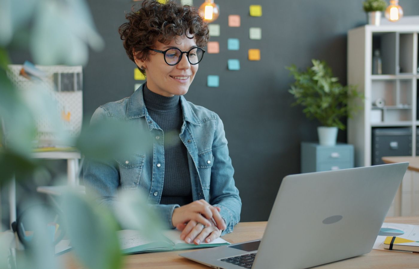 Confident woman in casual attire works on her laptop, seated in a stylish office setting.