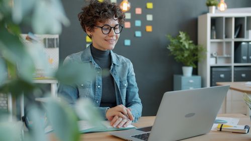 Free Confident woman in casual attire works on her laptop, seated in a stylish office setting. Stock Photo