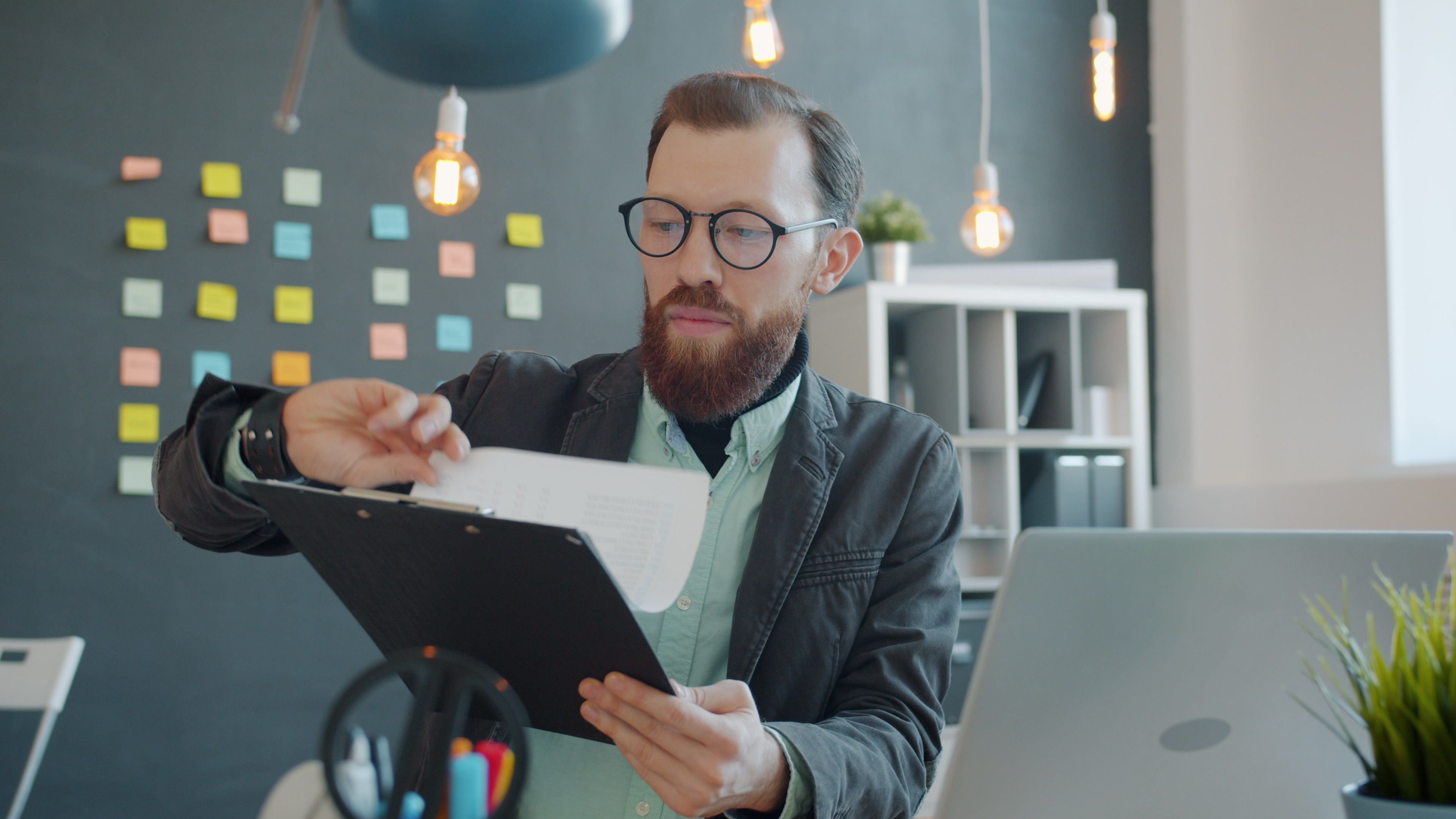 A focused young man with glasses reviewing documents in a stylish, modern office setting.
