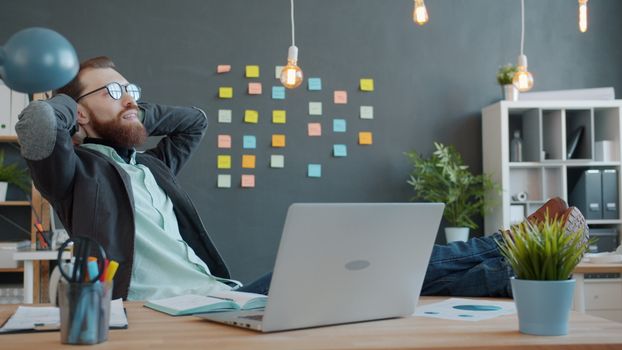 Young man relaxing in modern home office with laptop and sticky notes in background.