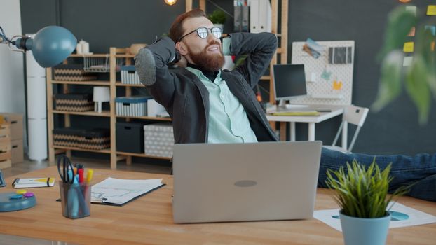 Young man relaxing at desk in modern office setting with laptop.