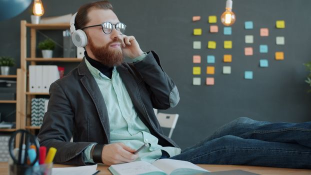 Casual man enjoying music on headphones in creative office space.