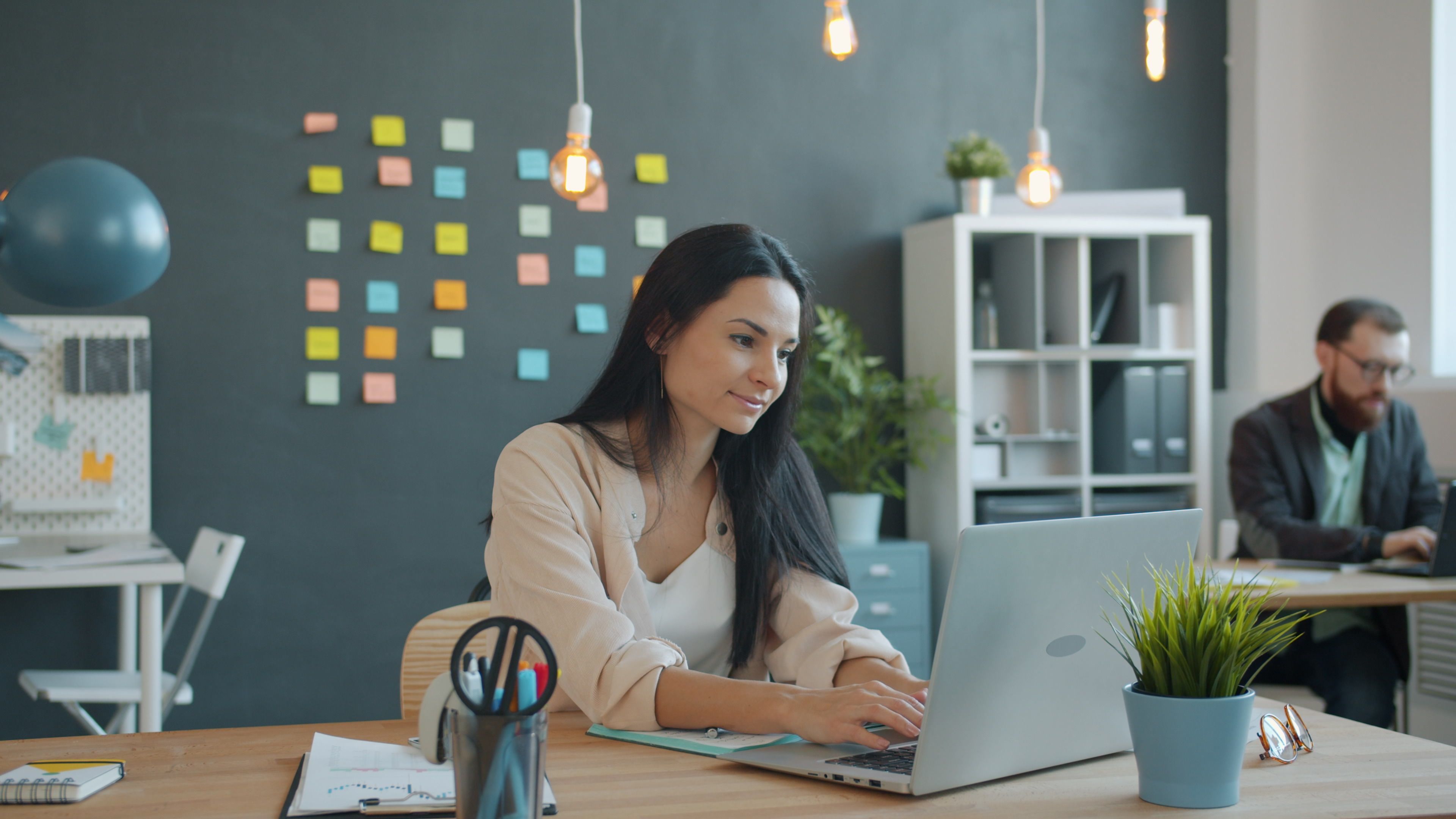 Two young adults working at laptops in a modern, creative office space.