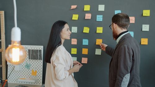 Free Two professionals brainstorming ideas using colorful sticky notes on a blackboard. Stock Photo