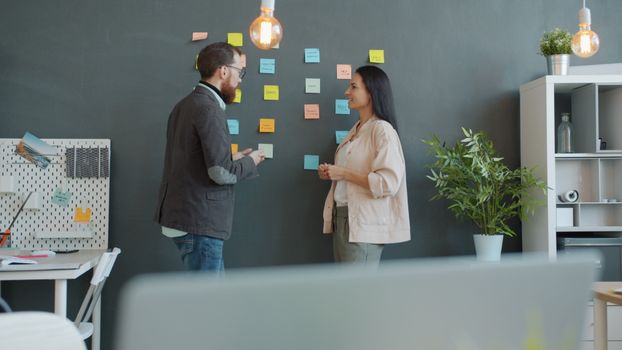 Two colleagues discussing ideas in a modern office using sticky notes on a wall.