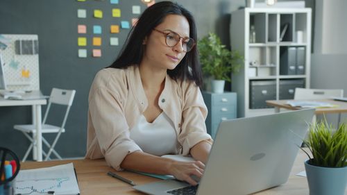 Free Focused woman typing on a laptop in a modern office setting. Stock Photo