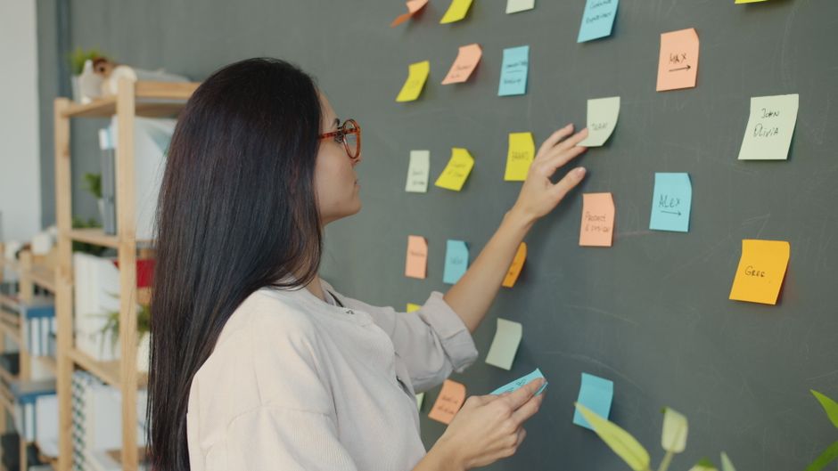 Woman placing colorful sticky notes on a blackboard in a modern office setting.