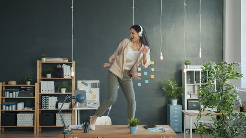 Free Happy woman dancing on office desk with headphones, expressing joy. Stock Photo