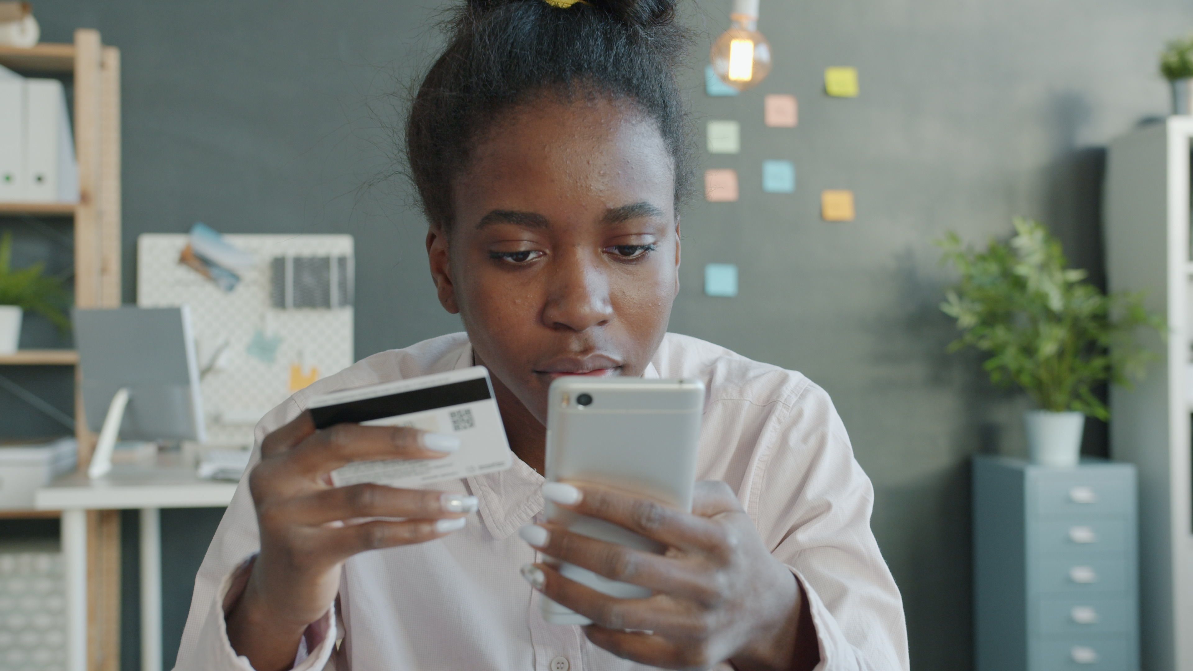 Focused woman using smartphone and credit card in modern office setting for online shopping.