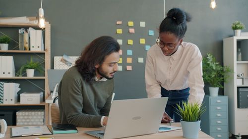 Free Two colleagues collaborating at a desk with laptop in a modern office space. Stock Photo