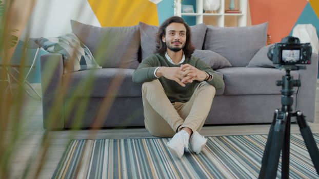 Young man sitting on the floor recording a vlog at home with a camera.