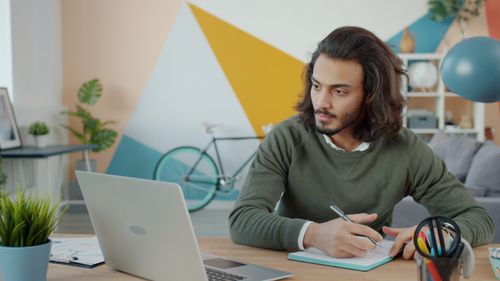 Free Focused young man takes notes while working on laptop from a home office. Stock Photo