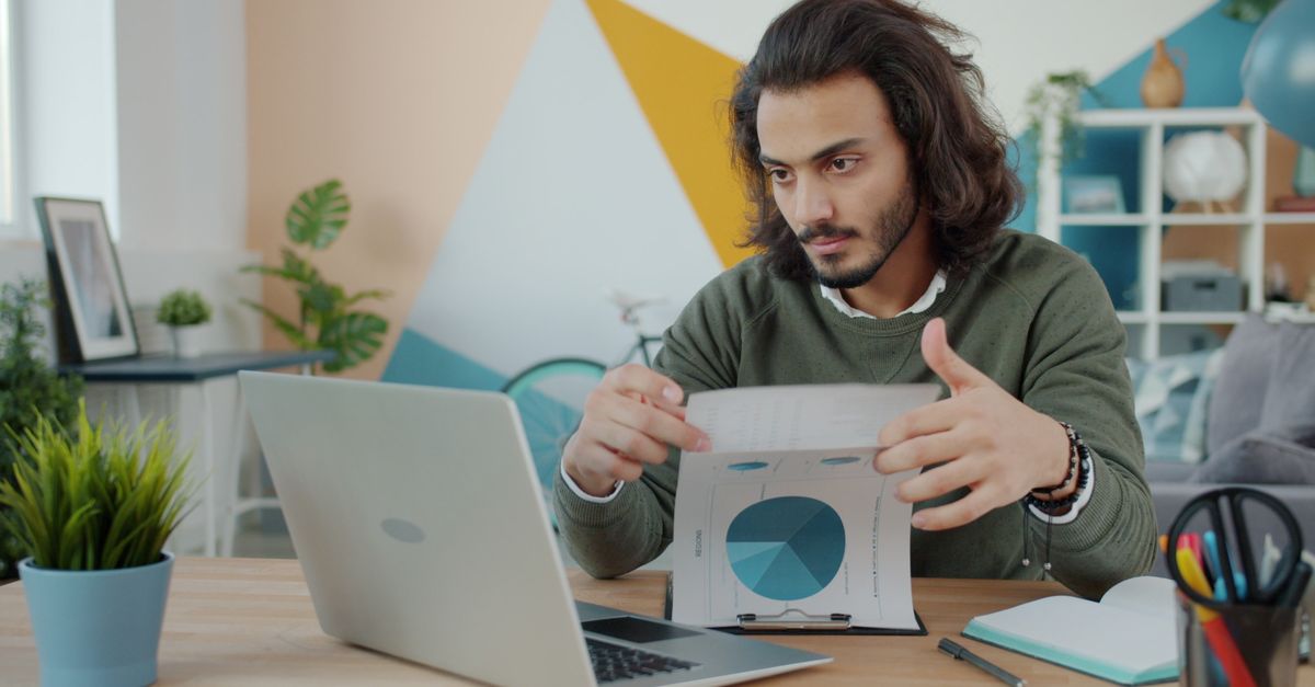 Jeune homme concentré analysant des graphiques financiers à son bureau à domicile.